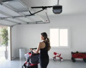 A woman pushes a stroller through a clean garage with an overhead LiftMaster door opener and a red tricycle in the background
